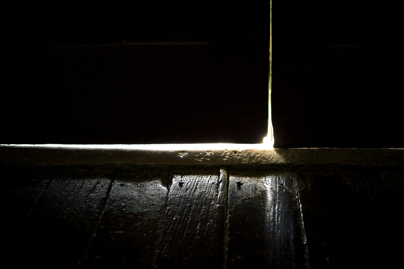Light slipping through a doorway onto a dark wooden floor
